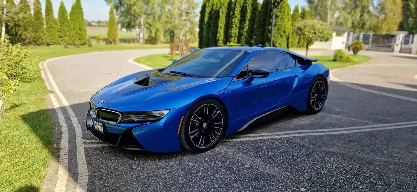 Błękitne BMW i8 na podjeździe salonu Kornak Motors, widok z przodu z boku